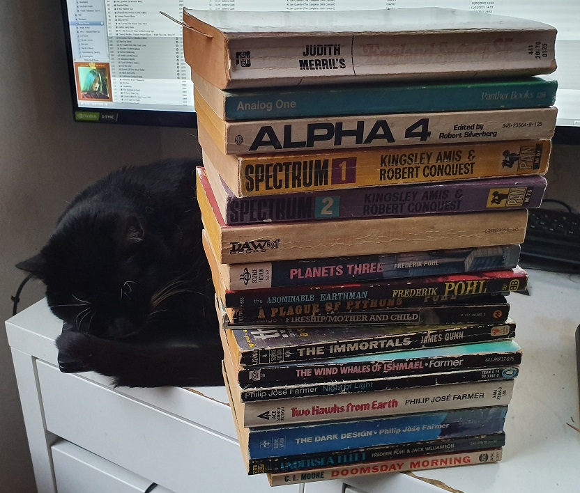 A stack of science fiction paperbacks with a cat sleeping behind it